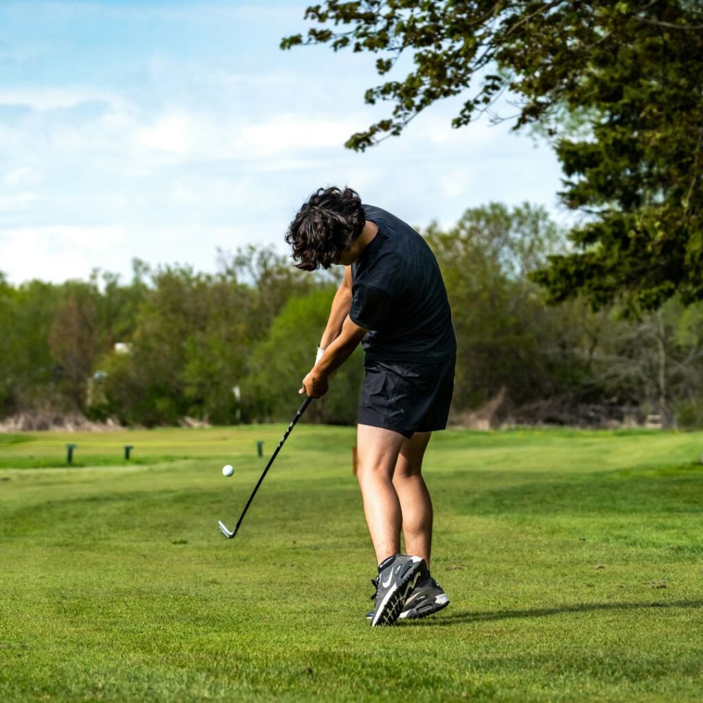 Golfer taking an approach shot on a scenic countryside golf course.