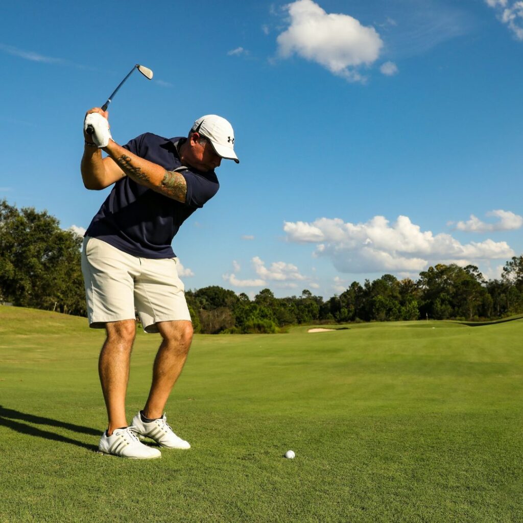 Golfer teeing off on a championship-style golf course under blue skies.