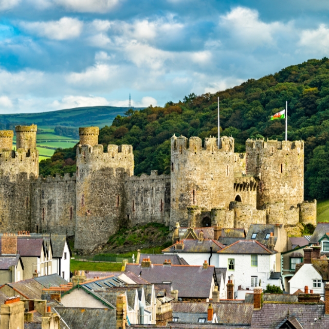 Conwy Castle’s stone towers rising above town rooftops, with wooded hills behind.