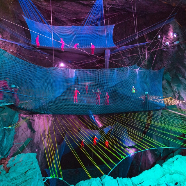 Colourful suspended bounce nets inside an illuminated slate cavern at Zip World Llechwedd.