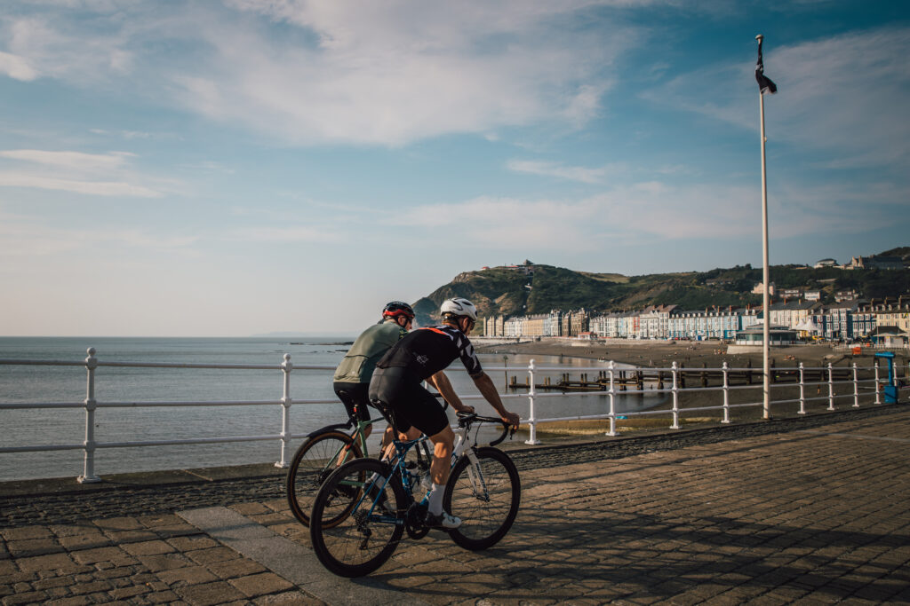 Two cyclists riding along a seaside promenade beside a sheltered bay.