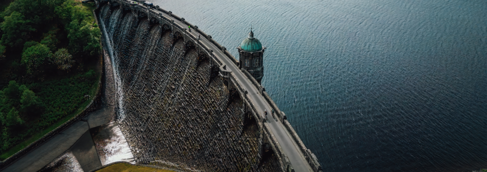 Aerial view of Lake Vyrnwy’s stone dam and reservoir, bordered by woodland.