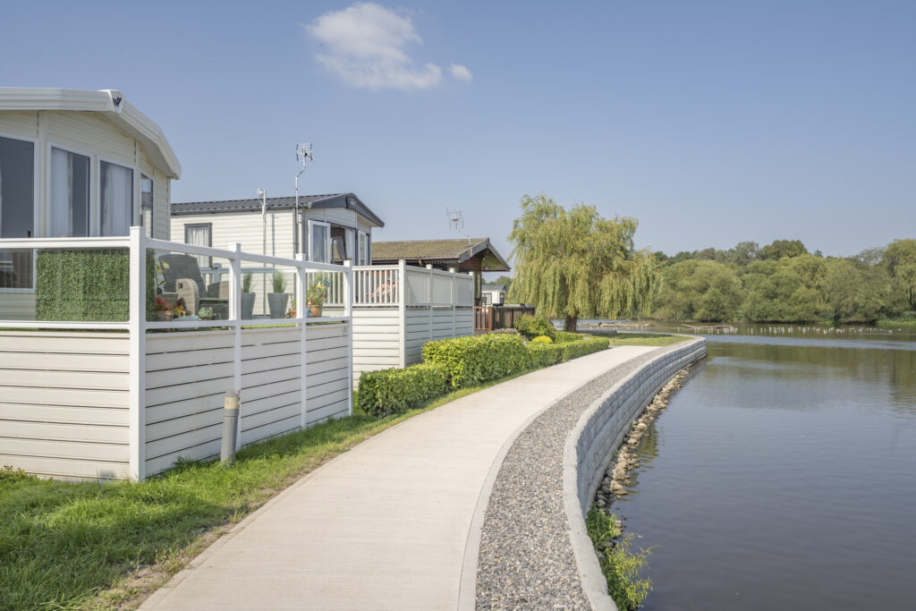 Holiday homes with raised decking beside a curved lakeside path at Lakeside Caravan Park.